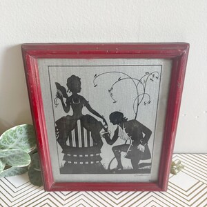 Puede incluir: Enmarcado arte de silueta con un marco rojo desgastado. La imagen en blanco y negro muestra a un hombre arrodillado ante una mujer. La obra de arte representa una escena rom&aacute;ntica. El marco es de forma cl&aacute;sica, ideal para decoraci&oacute;n vintage.