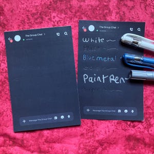 May include: Two black rectangular cards featuring a digital messaging interface design with the text The Group Chat. One card displays handwritten white ink text listing White, Black, Blue metal, Gold, Paint Pen, and Purple next to three pens.