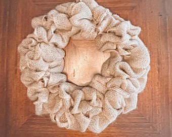 May include: A rustic burlap wreath with a natural, neutral color. The wreath is circular, with the burlap material gathered and layered to create a full, textured appearance. The wreath is a decorative item.