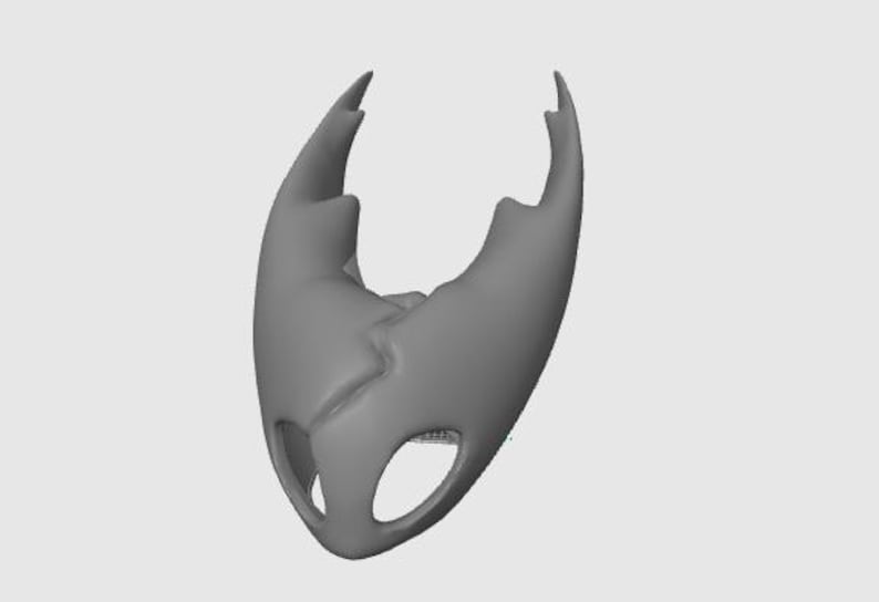 May include: A gray, stylized mask with a cracked design and two eye-shaped openings. The mask has two pointed protrusions at the top and a smooth, curved shape overall. The object is set against a plain, light gray background.