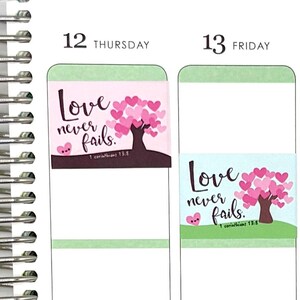 May include: Planner stickers with the text "Love never fails" and a tree with pink heart-shaped leaves. The stickers are rectangular and feature a light blue and pink background. The text "1 Corinthians 13:8" is also included.