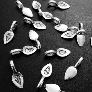 May include: A collection of silver-toned teardrop-shaped jewelry findings with small loops for attaching to other components. The teardrop pendants have a textured, dotted design on the front. The findings are scattered on a dark surface.