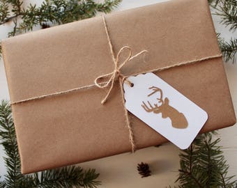 Könnte beinhalten: Ein braunes Geschenkpaket aus Papier, das mit Schnur gebunden ist und einen weißen Geschenkanhänger mit einer goldenen Silhouette eines Hirschkopfes.