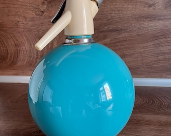 Pode incluir: Um sifão de soda vintage com um corpo de vidro turquesa redondo e uma parte superior e inferior creme. O sifão apresenta um dispensador cromado e uma alça preta. Um clássico da cozinha retrô.