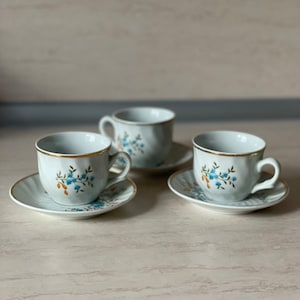 May include: Three white porcelain teacups with blue and orange floral designs and gold trim. Each cup is on a matching saucer.