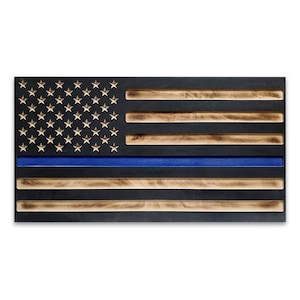 May include: Wooden American flag with a blue line, featuring gold stars and alternating dark and light brown stripes. The flag is a rectangular shape and appears to be made of wood.