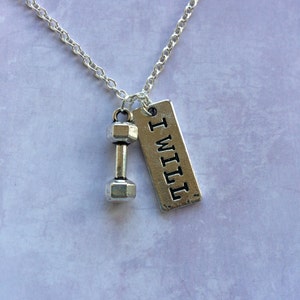 May include: Silver-colored necklace featuring a dumbbell charm and a rectangular tag. The tag is engraved with the words "I WILL" in capital letters. The necklace is on a silver chain, perfect for fitness enthusiasts.