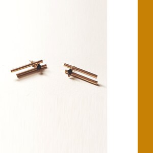 May include: A pair of minimalist gold bar earrings with black accents. The earrings are on a white background with the text "Minimalist Bar Earrings".