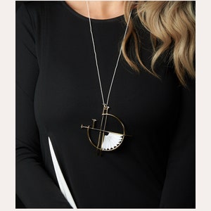 Puede incluir: Un collar de oro con un colgante geom&eacute;trico que presenta un dise&ntilde;o de abanico de papel blanco. El colgante est&aacute; suspendido de una fina cadena plateada. El collar lo lleva una persona con el pelo largo rubio y una camisa negra. El texto "MADE TO ORDER" est&aacute; en la parte superior de la imagen y el texto "SMALL THINGS THAT MAKE YOU FEEL SPECIAL" est&aacute; en la parte inferior de la imagen. El texto "Every day Look" est&aacute; centrado debajo del texto anterior.