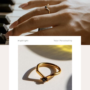 May include: A gold ring with a black stone set in the center. The ring is shaped like a V and is on a white surface.
