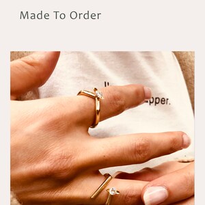 May include: Two gold rings with small clear stones. The rings are worn on the index and middle fingers of a hand.