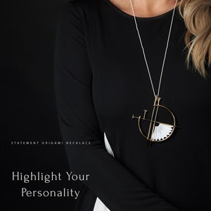 Puede incluir: Una mujer lleva una camisa negra con un collar de origami blanco. El collar est&aacute; hecho de papel doblado y tiene un marco de metal dorado. El texto "STATEMENT ORIGAMI NECKLACE" est&aacute; en la parte inferior izquierda de la imagen. El texto "Highlight Your Personality" est&aacute; en el centro de la imagen. El texto "THE MORNING AFTER" est&aacute; en la parte inferior central de la imagen.