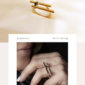 May include: A gold ring with two parallel bars and a black stone in the center. The ring is worn on a person's finger.