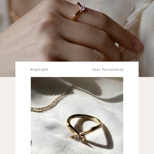May include: A gold ring with a small clear stone set in the center. The ring is shaped like a V and is shown on a white fabric background.