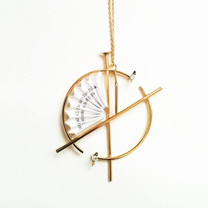 Puede incluir: Collar de oro con un dise&ntilde;o geom&eacute;trico que presenta un peque&ntilde;o abanico de papel con el texto "and all the days that follow I am near to you".
