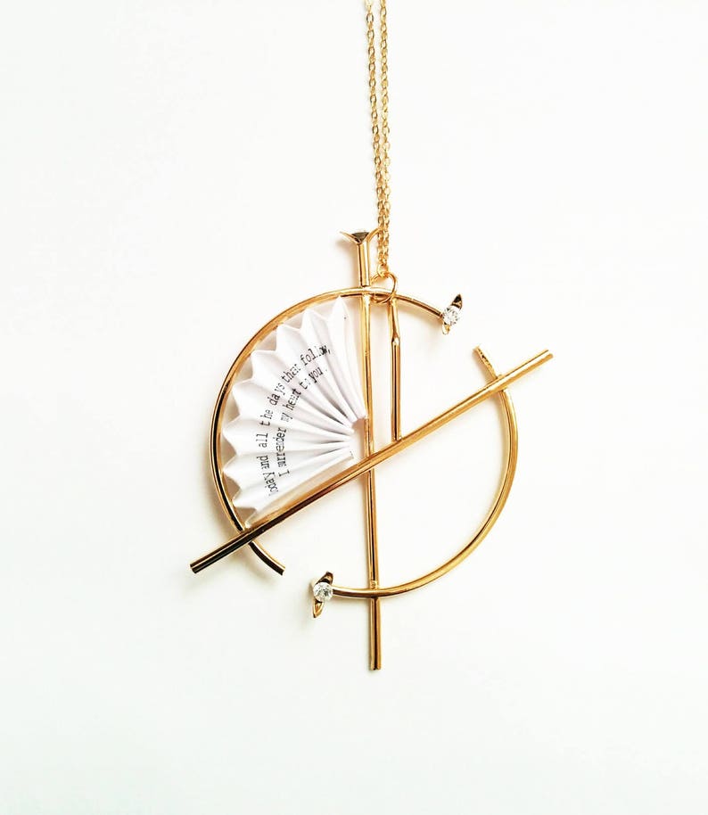 Puede incluir: Collar de oro con un dise&ntilde;o geom&eacute;trico que presenta un peque&ntilde;o abanico de papel con el texto "and all the days that follow I am near to you".