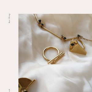 May include: Three gold rings with black stones. The rings are on a white fabric background. The rings are a bar ring, a triangle ring, and a half circle ring. The text "Every Day Look" and "Bar Ring" are on the left and right sides of the image.