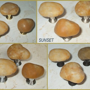 Könnte beinhalten: Nahaufnahme von fünf verschiedenen Ausführungen von Steinknöpfen. Die Knöpfe haben alle die gleiche Form, ein abgerundetes Oval, aber unterschiedliche Metalloberflächen. Die Oberflächen sind poliertes Gold, satiniertes Nickel, poliertes Chrom, geöltes Bronze und Sonnenuntergang.