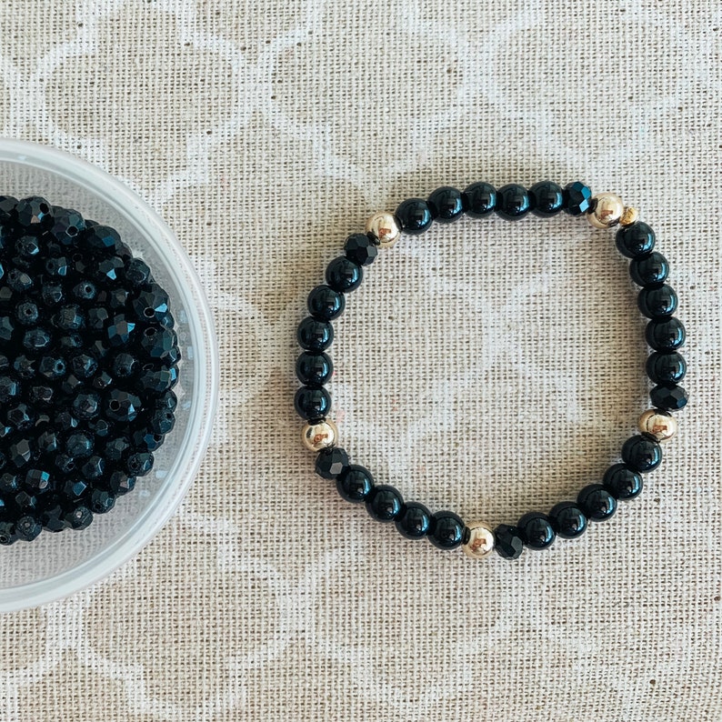 May include: A black beaded bracelet with gold accents. The bracelet is made of small, round beads and has a simple, elegant design.