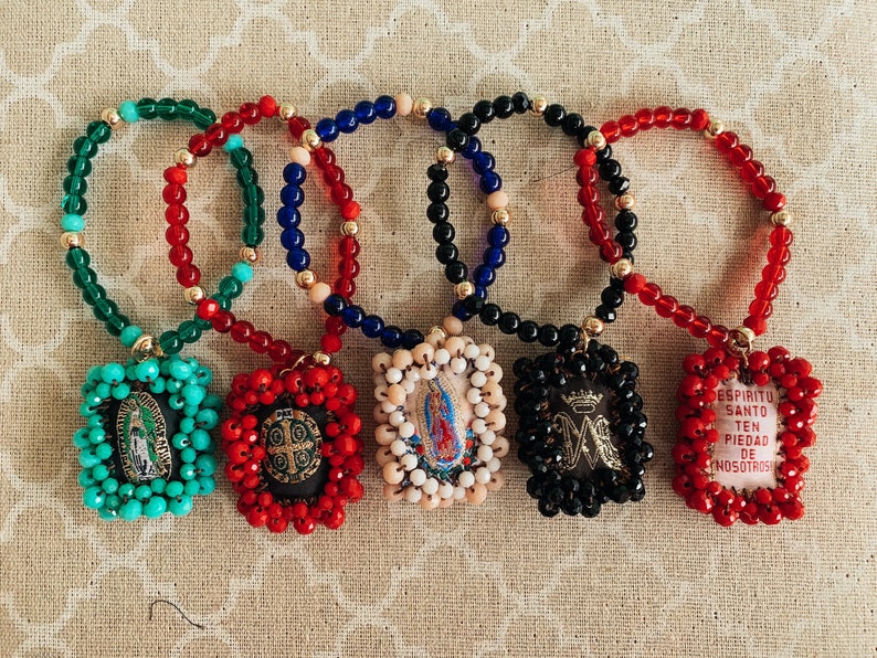 May include: Five colorful beaded bracelets with religious charms. Each charm is a different color and features a different religious image. The charms are surrounded by beads in the same color as the charm.