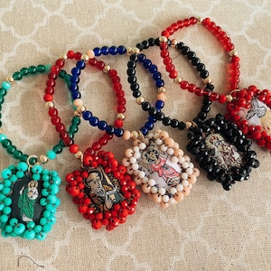 May include: Six colorful beaded bracelets with religious charms. Each bracelet features a different color of beads and a charm with a religious image.