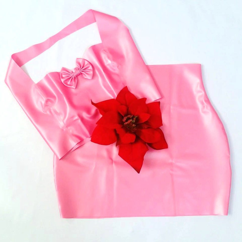 May include: A pink satin outfit consisting of a top with a bow detail and a matching skirt. A large red poinsettia flower is placed on the outfit. The top has a halter-style neckline.