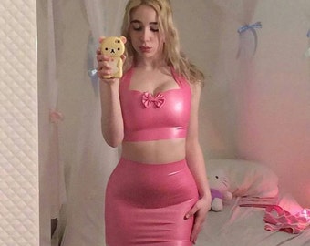 May include: A pink latex two-piece outfit, consisting of a halter top with a bow detail and a matching mini skirt. The outfit is shiny and form-fitting, creating a cohesive look. The overall aesthetic is bold and eye-catching.