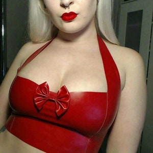 May include: A vibrant red halter top with a bow detail. The top is made of a shiny material and features a bow in the center. The halter straps are thin and the top is form-fitting.