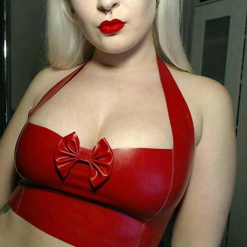 May include: A vibrant red halter top with a bow detail. The top is made of a shiny material and features a bow in the center. The halter straps are thin and the top is form-fitting.