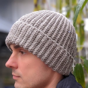 Puede incluir: Un gorro de punto gris y blanco con textura de canalé. El gorro lo lleva puesto una persona con una chaqueta azul oscuro.