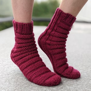 Könnte beinhalten: Ein Paar burgunderfarbene Stricksocken mit Rippenmuster. Die Socken sind knöchelhoch und haben eine bequeme Passform.