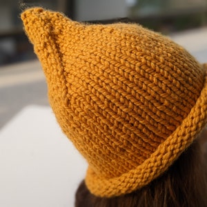 May include: A mustard yellow knitted beanie hat with a rounded crown and a folded brim.