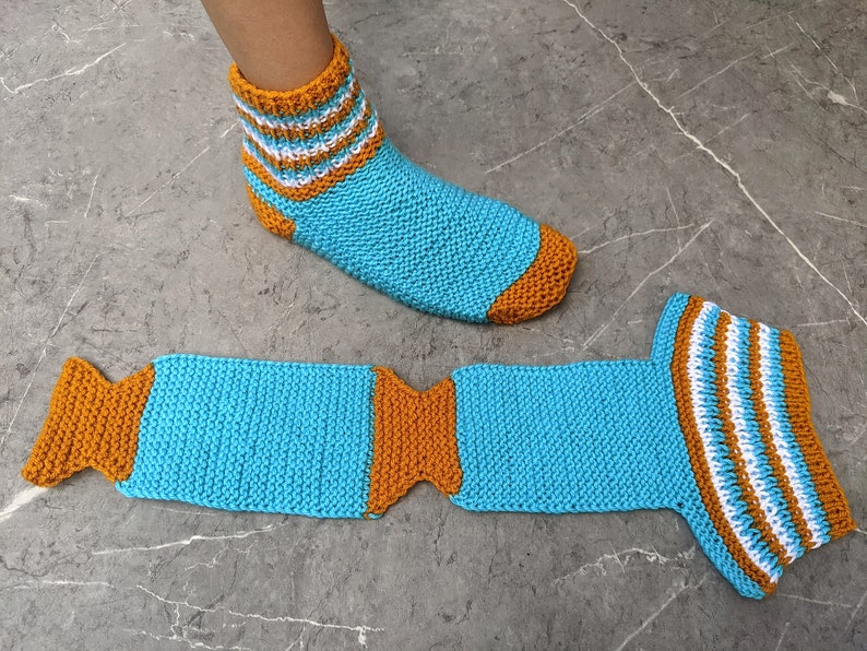 Puede incluir: Un par de calcetines de punto a rayas azules y naranjas. Un calcet&iacute;n est&aacute; en un pie y el otro est&aacute; puesto plano.