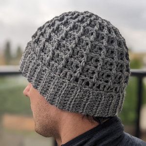 Puede incluir: Un gorro de punto de color gris con un patrón texturizado. El gorro lo lleva puesto una persona, pero su rostro no es visible.