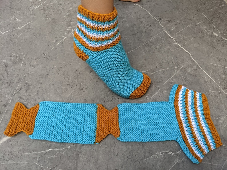 Puede incluir: Un par de calcetines de punto a rayas azules y naranjas. Un calcet&iacute;n est&aacute; en un pie y el otro est&aacute; puesto plano.