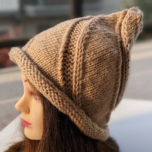 Puede incluir: Un gorro de punto marrón con un diseño único. El gorro tiene un ala ancha y una corona puntiaguda. El gorro está hecho de un hilo suave y cálido.