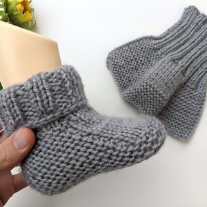 Könnte beinhalten: Ein Paar graue gestrickte Babyschuhe mit Umschlag.