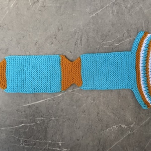 Puede incluir: Una bufanda de punto azul y naranja con rayas blancas. La bufanda est&aacute; hecha de hilo y tiene una forma larga y delgada.