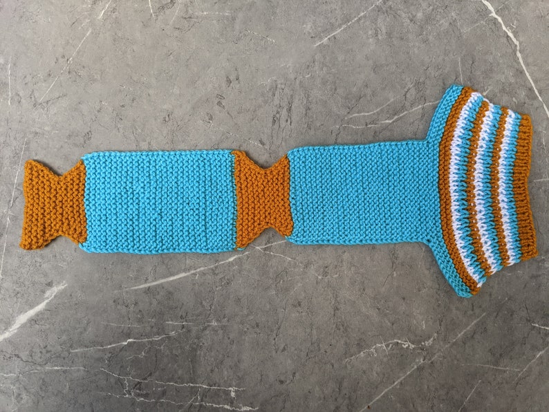 Puede incluir: Una bufanda de punto azul y naranja con rayas blancas. La bufanda est&aacute; hecha de hilo y tiene una forma larga y delgada.
