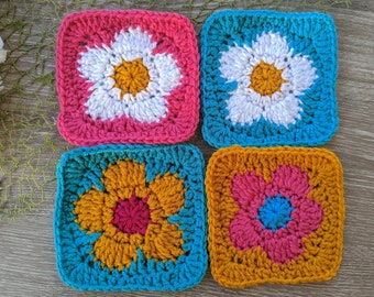 May include: Four crocheted squares with different coloured flowers in the centre. The squares are pink, blue, yellow, and red.