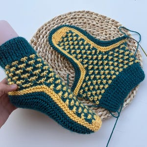 Op de afbeelding: Een paar handgebreide enkelsokken met een mozaïekpatroon in blauwgroen en geel. De sokken hebben een geribbelde boord, een verstevigd hiel- en teengedeelte in het geel en een gestructureerd steekpatroon over het gehele breiwerk.