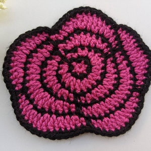 Könnte beinhalten: Eine gehäkelte Blume in Pink und Schwarz mit einem Spiralmuster.