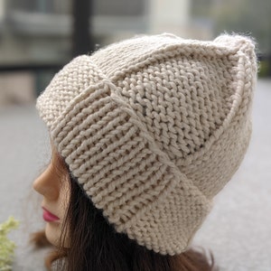 May include: A beige knitted beanie with a unique stitch pattern. The beanie is made of a soft, warm yarn and has a slouchy fit.