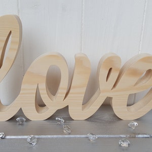 May include: A wooden sign spelling out the word "love" in a cursive font. The sign is made of natural wood and has a light brown color.