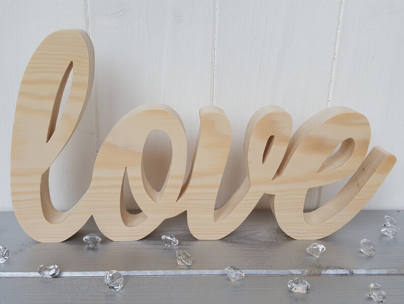 May include: A wooden sign spelling out the word "love" in a cursive font. The sign is made of natural wood and has a light brown color.