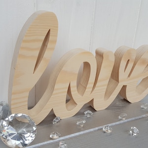 May include: Wooden cutout of the word "love" in a cursive font. The letters are freestanding and made of natural light wood.