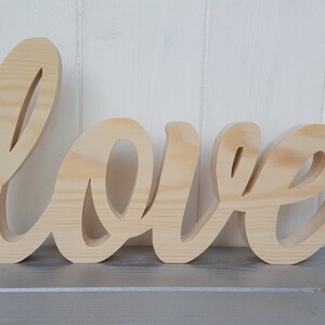 May include: A wooden sign with the word "love" written in a cursive font. The sign is made of natural wood and has a light brown color.