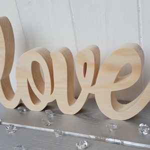 May include: A wooden sign spelling out the word "love" in a cursive font. The sign is made of natural wood and has a rustic look.