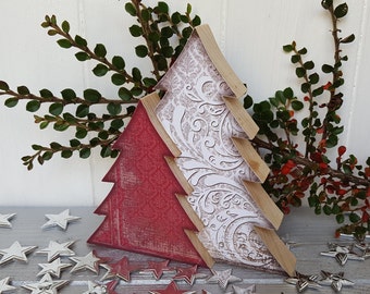Puede incluir: Dos adornos de árbol de Navidad de madera, uno rojo y otro blanco con un patrón decorativo. Los adornos están superpuestos y se encuentran sobre una superficie gris con estrellas plateadas.