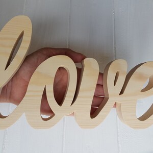May include: A wooden sign spelling out the word "love" in a cursive font. The sign is made of light brown wood and has a natural finish.